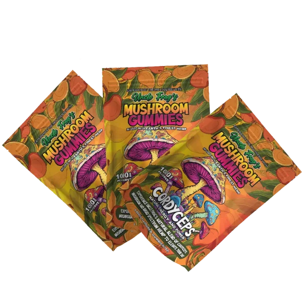 Three packets of "Uncle Frog's Mushroom Gummies" are displayed with a psychedelic and colorful design showcasing mushroom illustrations. The packets are emblazoned with promises of "Natural Energy and Power" from an "Experience the Multiverse" blend, and highlight "1000 mg Active PER SERVE" of hemp infusion. The mango flavor is featured, indicating a tropical taste experience.